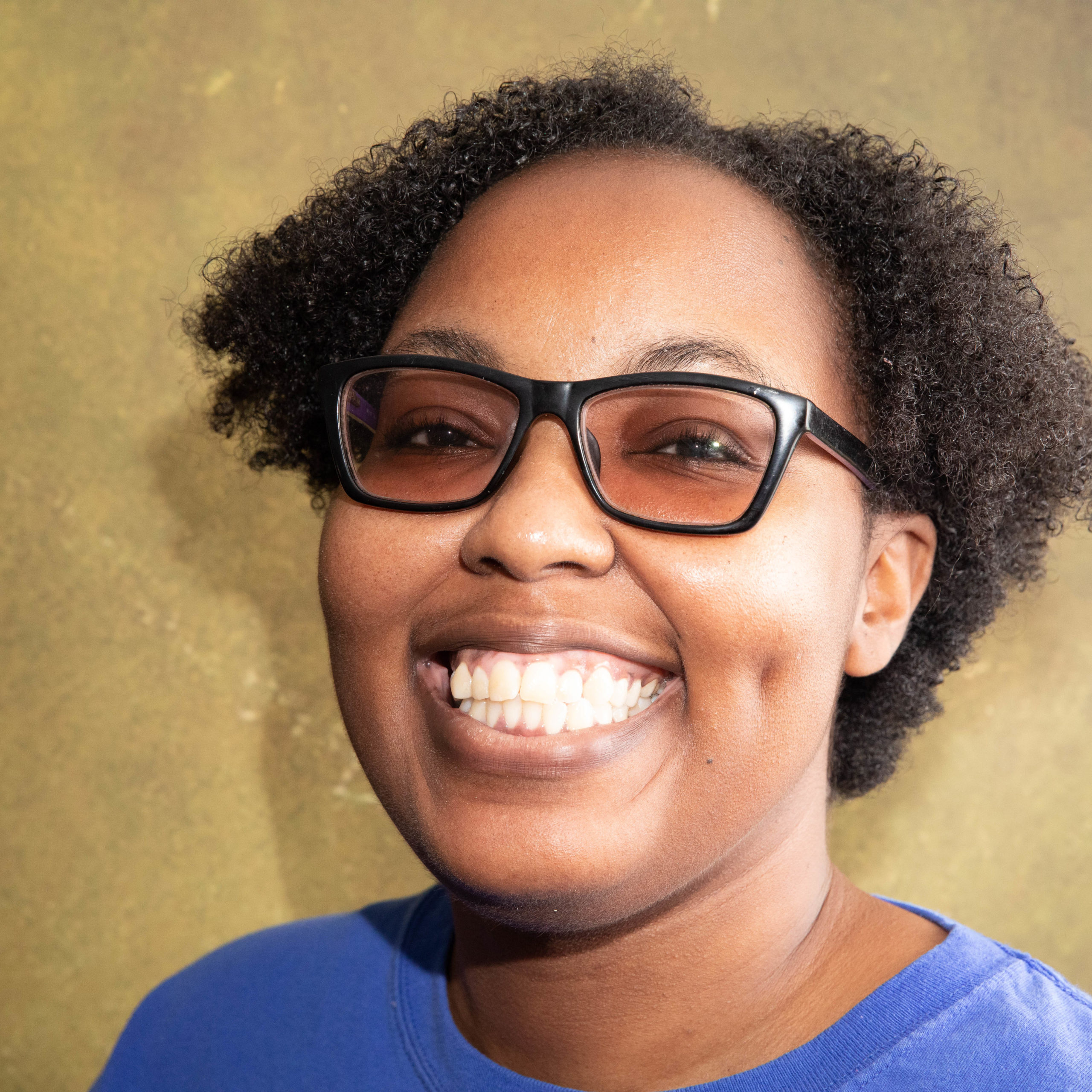 A person smiles wearing glasses and a blue shirt.